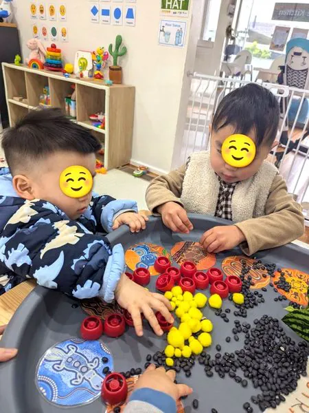 Two children sorting red, yellow and black loose parts on a sensory tray