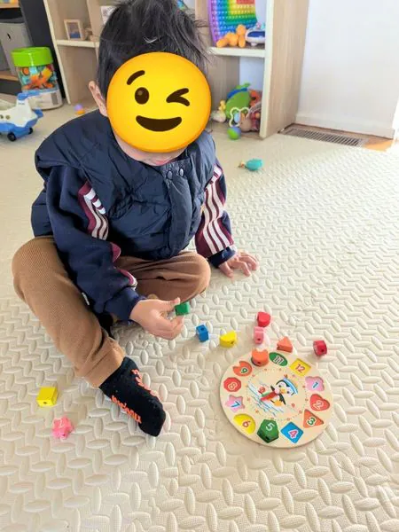 A toddler playing with a wooden shape-sorting clock